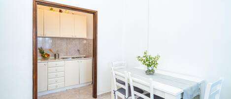 A compact kitchen with white cabinets, a sink, and a dining area with a table and chairs.