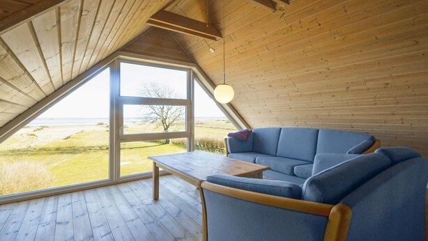 Une pièce chaleureuse avec un plafond en bois, une grande fenêtre et un canapé bleu.