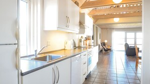 Une cuisine lumineuse avec des meubles blancs, un évier en acier inoxydable et un plafond en bois.