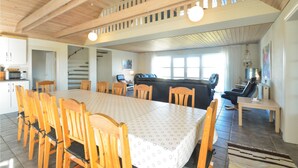 Un vaste espace de vie doté d’un haut plafond, de poutres apparentes, d’une table à manger avec des chaises, d’un canapé et d’un escalier menant à un niveau supérieur.