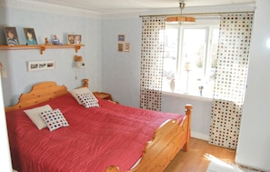 A bedroom with a wooden bed, red bedding, a shelf with photos, and a window with polka dot curtains. - Awesome home in Sölvesborg with kitchen (Sölvesborg)