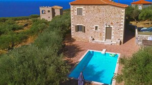 Un bâtiment en pierre doté d’une piscine, d’une tour et offrant une vue sur la mer.