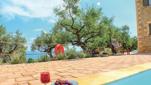 Un espace aménagé au bord de la piscine, avec vue sur la mer, un parasol rouge et des sièges d’extérieur.