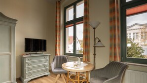 A room with a television on a dresser, two chairs around a table, and a window with curtains.