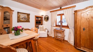 Une pièce chaleureuse avec un plafond en bois, une table à manger avec des chaises, une bibliothèque, un canapé blanc, un meuble en bois et une fenêtre avec des rideaux.
