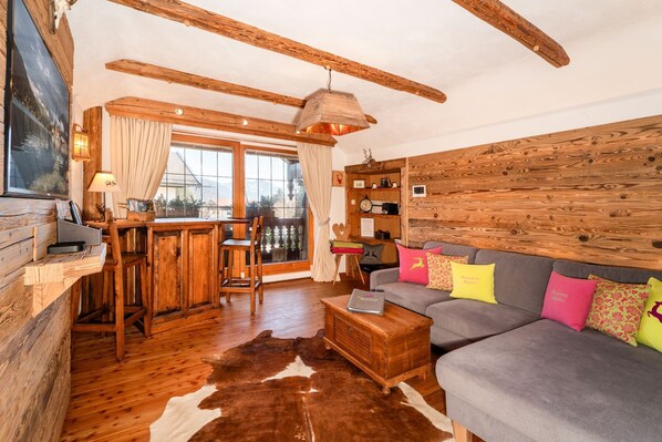 A rustic living room with wooden beams, a sofa with colorful cushions, a wooden coffee table, and a cowhide rug.