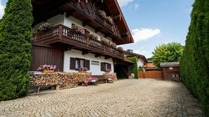 Un chalet traditionnel avec des balcons en bois, une allée pavée et une pile de bois de chauffage soigneusement rangée.