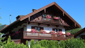 Un chalet traditionnel doté d’un balcon en bois, de murs blancs et de fleurs roses.