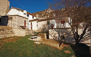 Ein Steinhaus mit kleinem Garten, einer Holztreppe und einem Balkon mit Blumentopf.