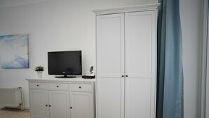 A room with a white wardrobe, a television on a cabinet, a radiator, and a blue curtain. - Holiday apartment Granitz (A) - Apartment house "Haus Arkona" (Sellin)