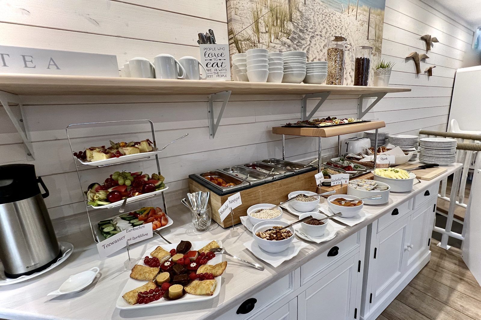 Dispositiu de buffet amb diferents aliments i utensilis, incloent una zona de cafè i un cartell que diu 'Pessoas que forçam a comer sempre são as melhores pessoas'.