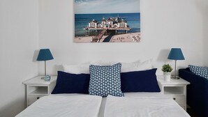 A bedroom with a bed, two nightstands, two lamps, and a wall-mounted picture of a pier and buildings by the sea. - Holiday apartment Granitz (A) - Apartment house "Haus Arkona" (Sellin)