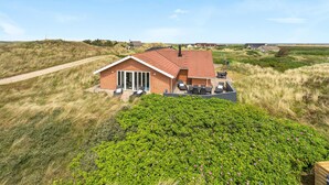 Uma casa térrea de tijolos com telhado vermelho, um pátio com móveis de exterior e vista para a paisagem ao redor.