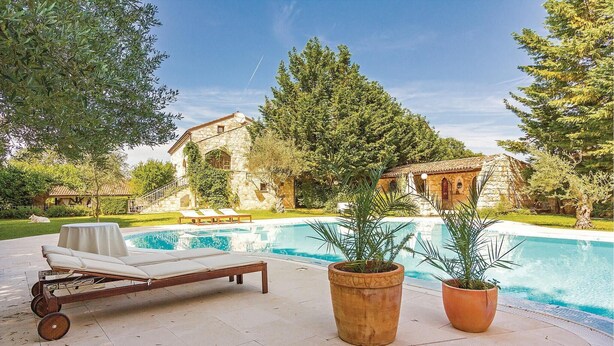 Un espace aménagé au bord de la piscine, avec un fauteuil de relaxation, deux plantes en pot et un bâtiment en pierre en arrière-plan.