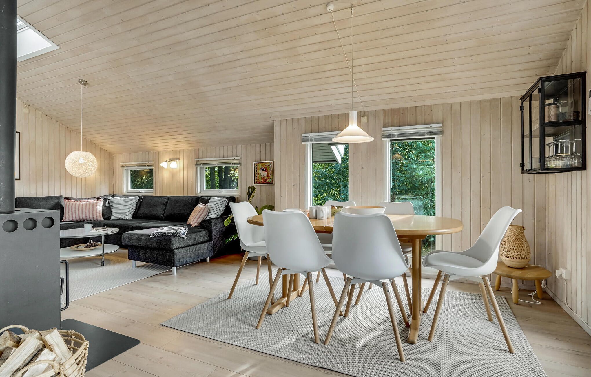 En moderne stue med en sort sofa, hvide stole, et træspisebord og store vinduer.