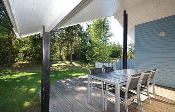 A covered patio with a wooden deck, a table with chairs, and a view of a backyard with trees. - Nice home in Væggerløse with sauna (Væggerløse)
