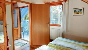 Un dormitorio con puerta de madera, ventana con cortinas, radiador y cama con manta a rayas.