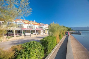 A waterfront hotel with outdoor seating, a paved walkway, and a view of the water.