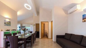 Un soggiorno moderno con un divano scuro, un'area pranzo con un tavolo apparecchiato per quattro persone e una cucina sullo sfondo.