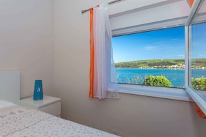 A bedroom with a window overlooking a body of water and greenery.