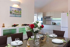 A dining area with a table set for four, a vase with flowers, and a painting on the wall.