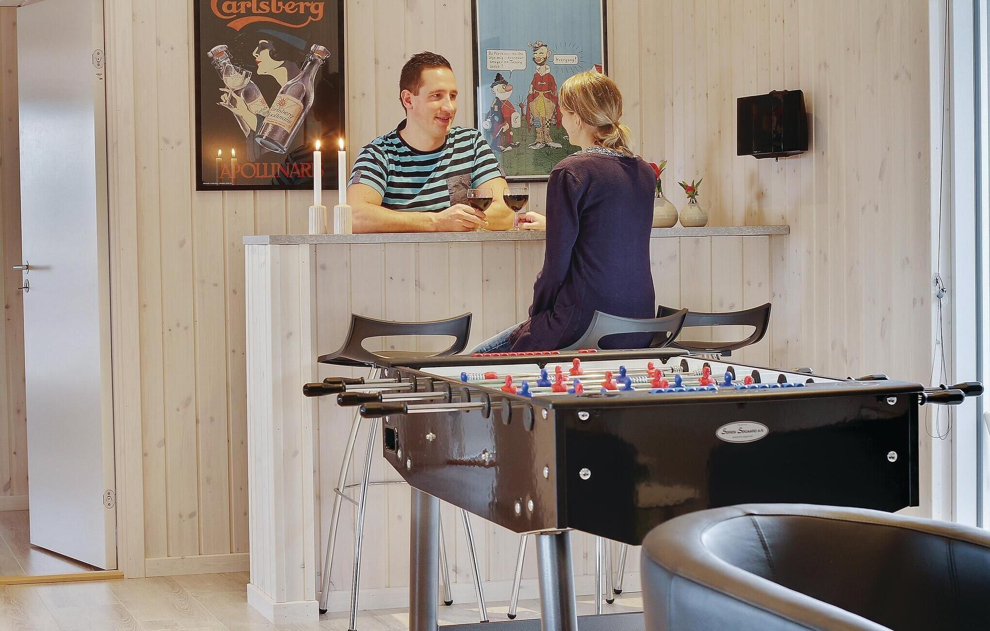 Ein Raum mit einem Kicker, einer Bar mit einem Poster und einer Holzwand.