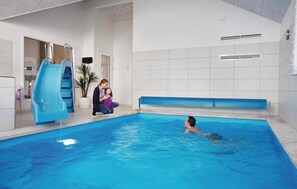 An indoor swimming pool with a blue slide, a child swimming, and two adults watching.
