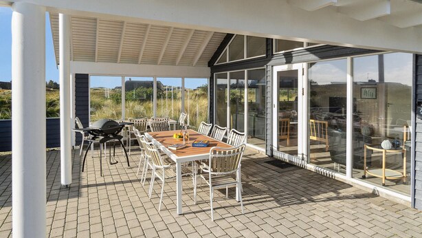 Eine Terrasse im Freien mit Tisch und Stühlen, einem Grill und einer Glaskonstruktion mit Blick auf die Landschaft.
