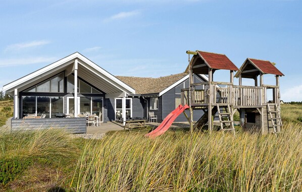 A modern house with a large patio, a wooden play structure, and a red slide.