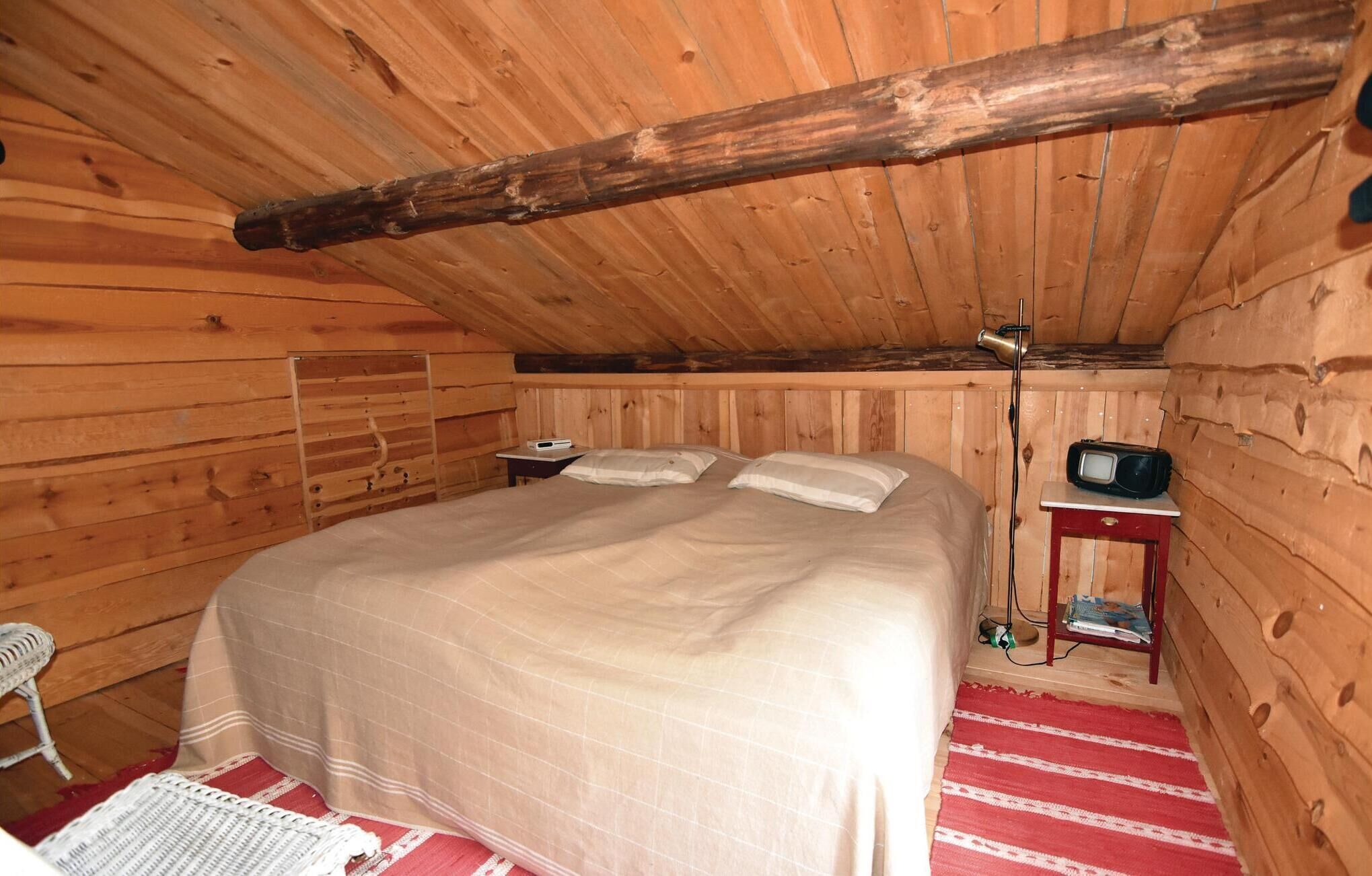 A wooden cabin room with a bed, a small table, a radio, and a chair.