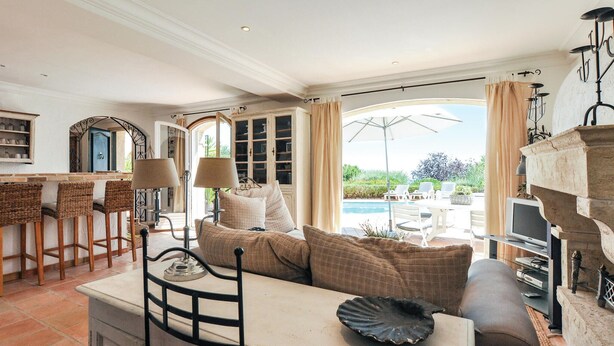 A spacious living area with a sofa, a dining table with chairs, a TV, and a view of a pool and garden. - Cozy home in Les Adrets d l'Estérel (Les Adrets d l'Estérel)