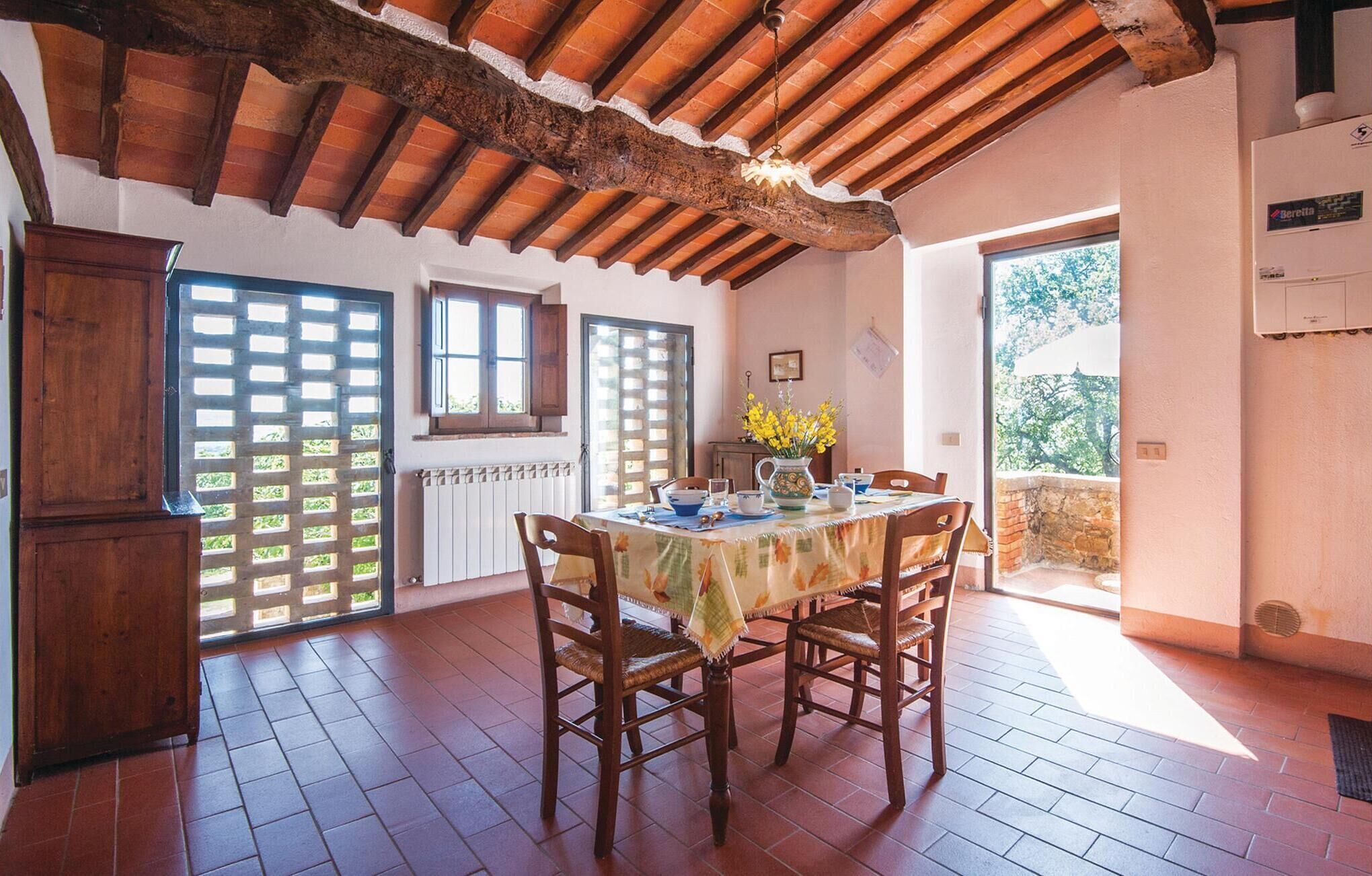 A dining area with a rustic wooden ceiling, a table set with chairs, and a view of the outdoors through a door.