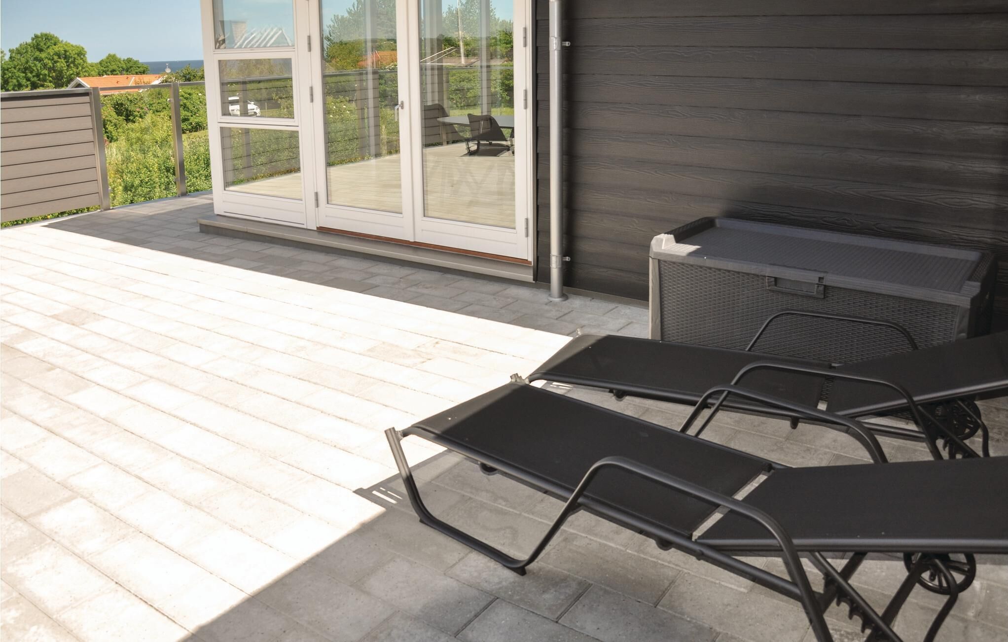 En udendørs terrasse med træterrasse, grill og to liggestole.