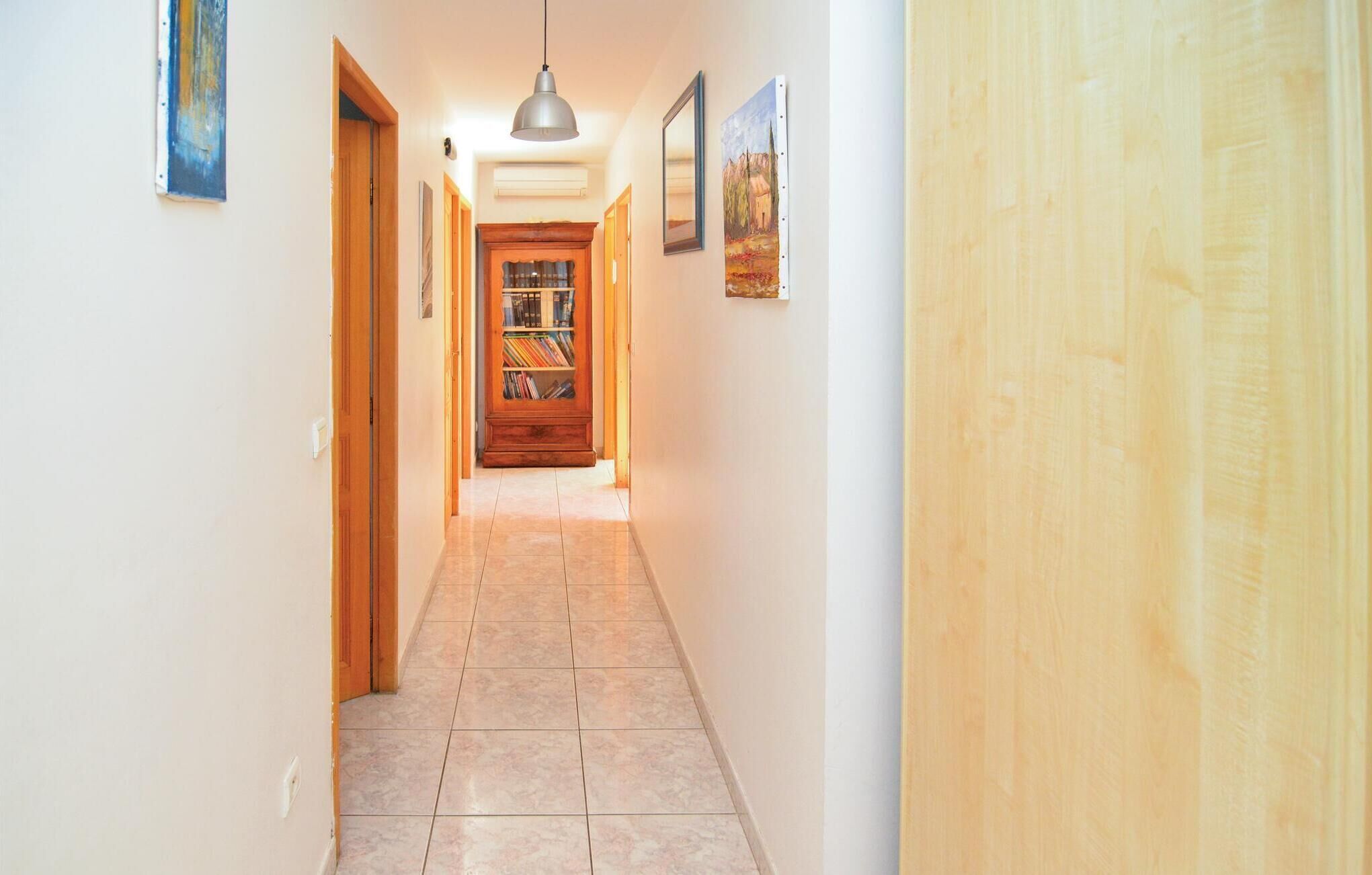 A hallway with a wooden door at the end, a bookcase, and a painting on the wall.