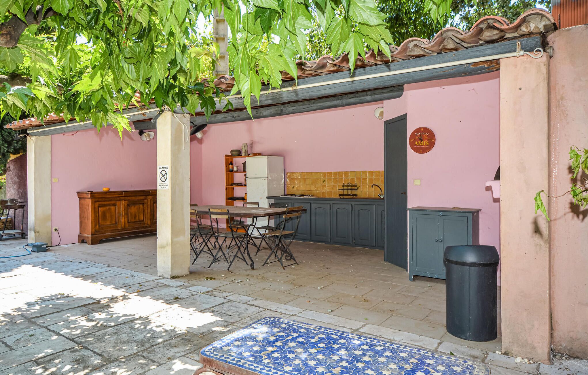 A small, enclosed outdoor kitchen area with a table and chairs, a refrigerator, and a tiled backsplash.