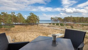 Ein Balkon mit Tisch und Stühlen mit Blick auf Strand und Wald.