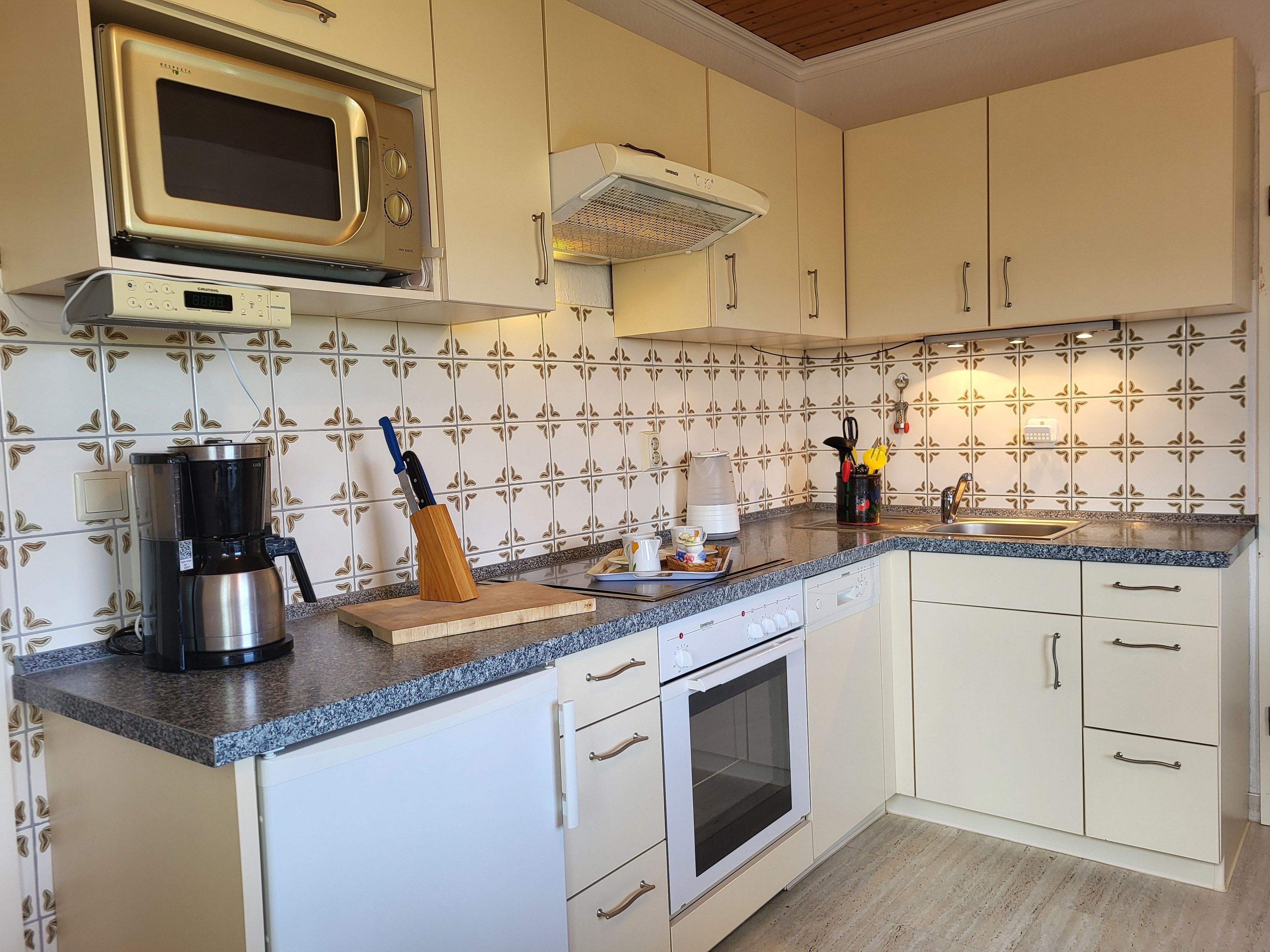 Una cocina con gabinetes blancos, microondas, cafetera y bloque de cuchillos.