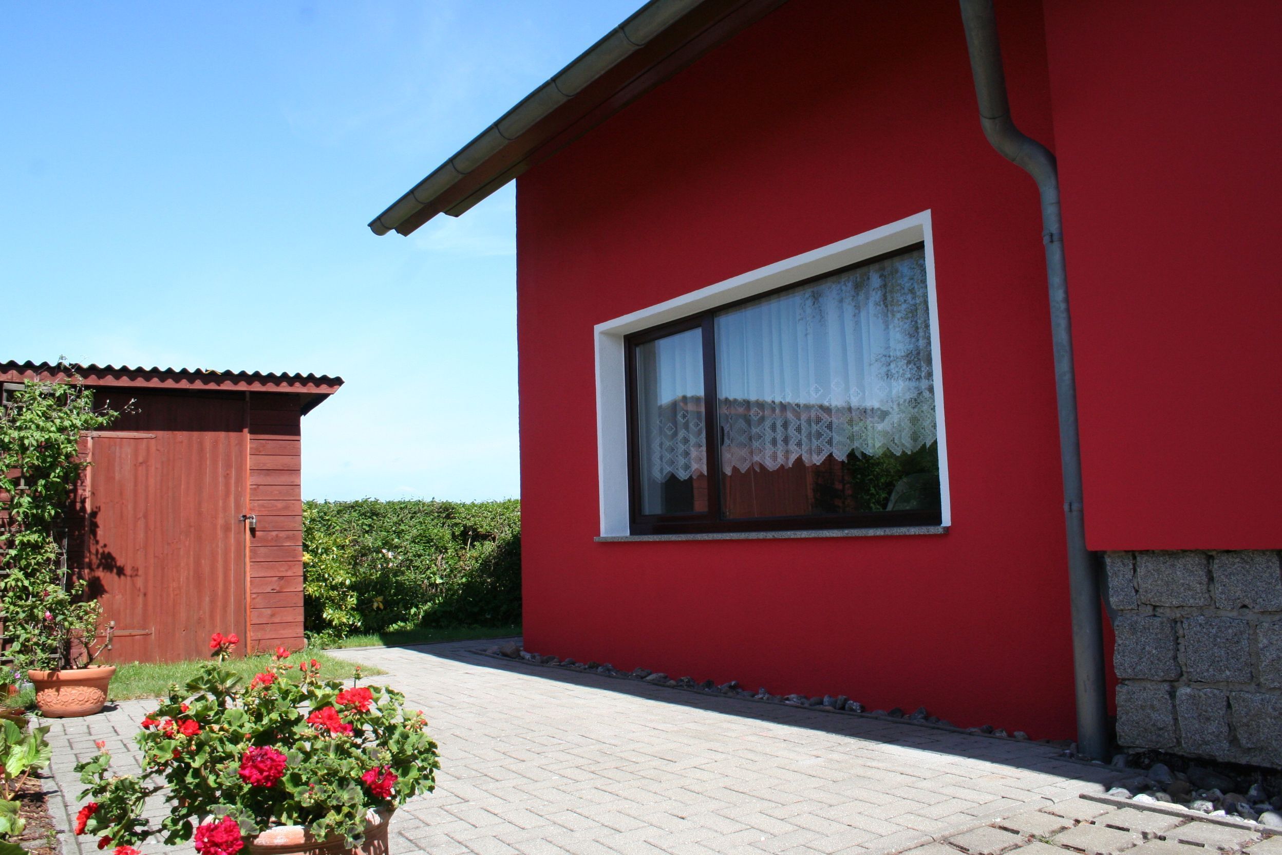 A red building with a window, a door, and a paved path.