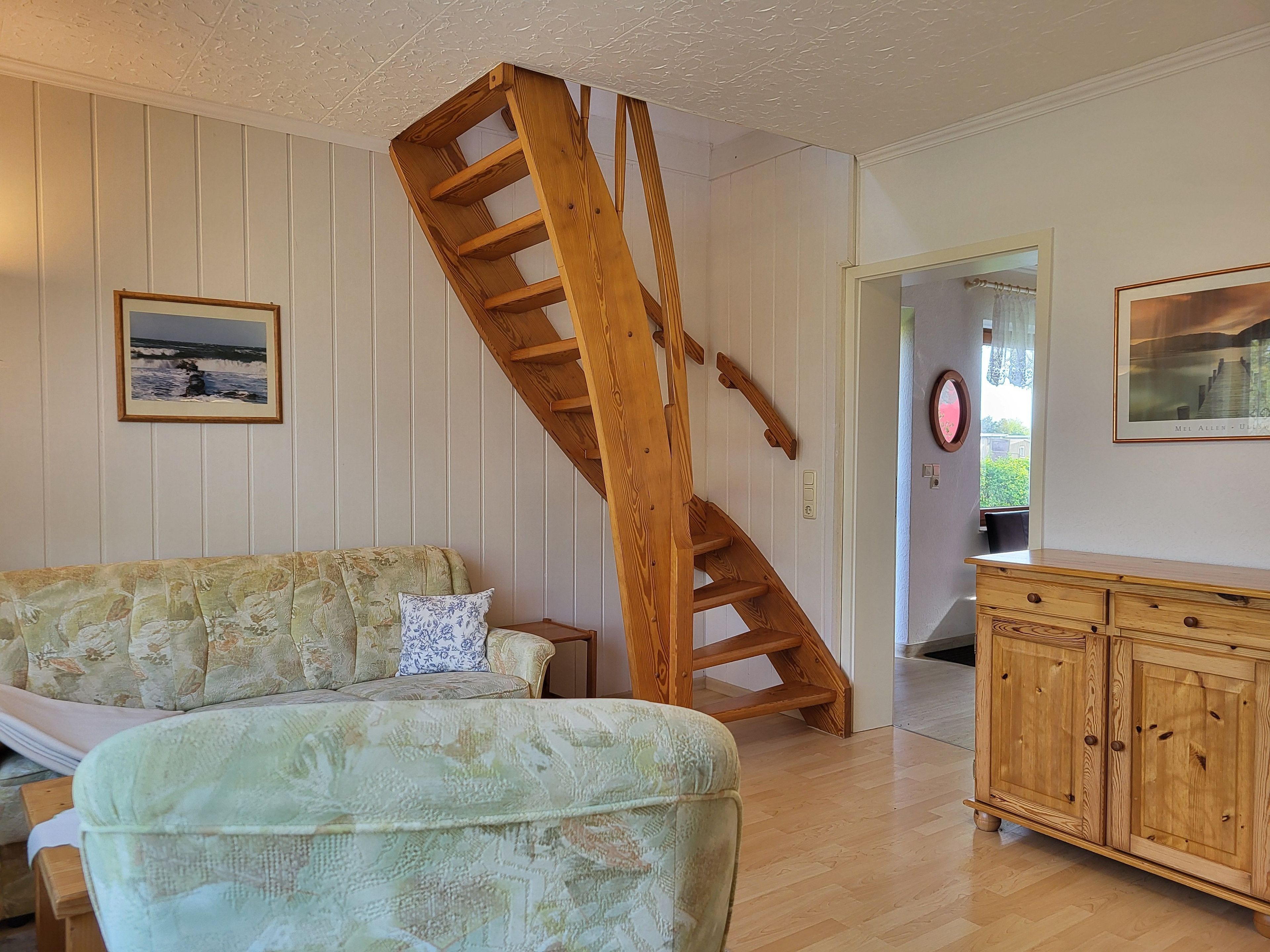 A living room with a wooden staircase, a sofa, a wooden cabinet, and framed pictures on the walls.