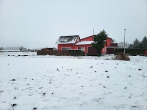 Une maison rouge avec un toit en pente, entourée d’un champ recouvert de neige.