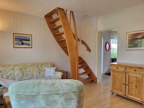 A living room with a wooden staircase, a sofa, a wooden cabinet, and framed pictures on the walls.