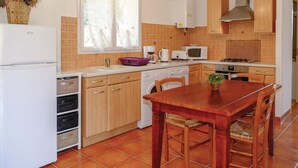 Cocina compacta equipada con lavavajillas, microondas y estufa. Cuenta con una mesa de comedor con sillas y una ventana con cortinas.