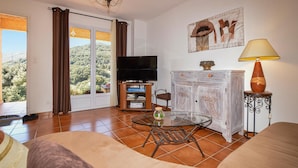 Una sala de estar con televisor, una mesa de vidrio, un aparador y un sofá.