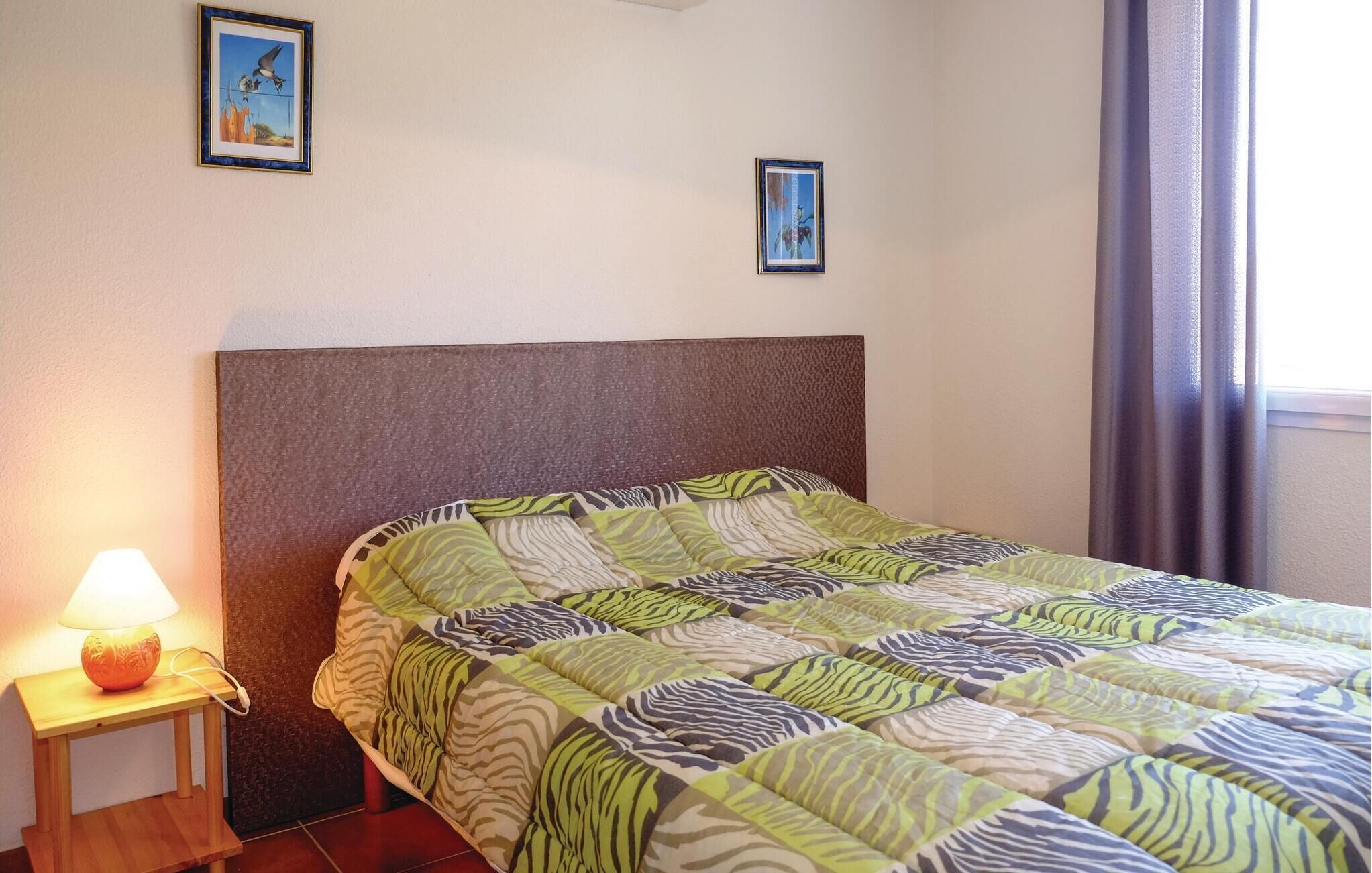 Een netjes opgemaakt bed met een bedspreider met zebraprint, een klein nachtkastje met een lamp en twee ingelijste foto's aan de muur.