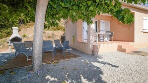 Un patio con mobiliario exterior, una parrilla y un edificio con puerta y ventanas.