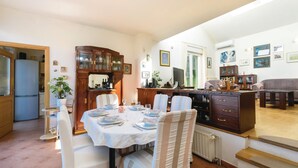 Un comedor con una mesa lista para cuatro, una cocina con refrigerador y una sala de estar con sofá y televisor.