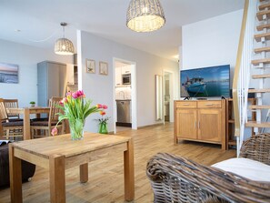 Un salon moderne avec une table à manger en bois, un téléviseur posé sur un meuble en bois et un fauteuil en osier.