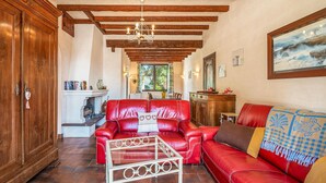 A cozy living room with a red leather sofa, a glass coffee table, wooden beams on the ceiling, and a fireplace. - Stunning home in Les Moutiers En Retz (Les Moutiers En Retz)