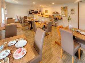 Un espace repas avec des tables et des chaises, une cuisine à l’arrière-plan et une affiche accrochée au mur.