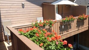 Eine Holzterrasse mit Holzgeländer, einem weißen Sonnenschirm und roten Blumen.